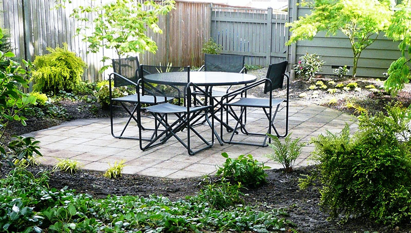 Patio of 12- by 12-inch sand-set concrete pavers sits amid plantings.