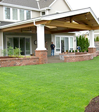 View from far fence corner towards the new patio, its cover, and the raised planters and seat wall